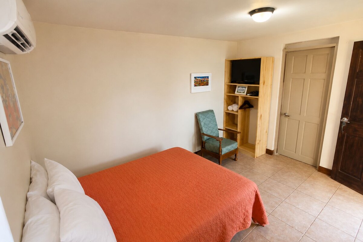 A bedroom with a bed, a chair, a wardrobe, and a door.
