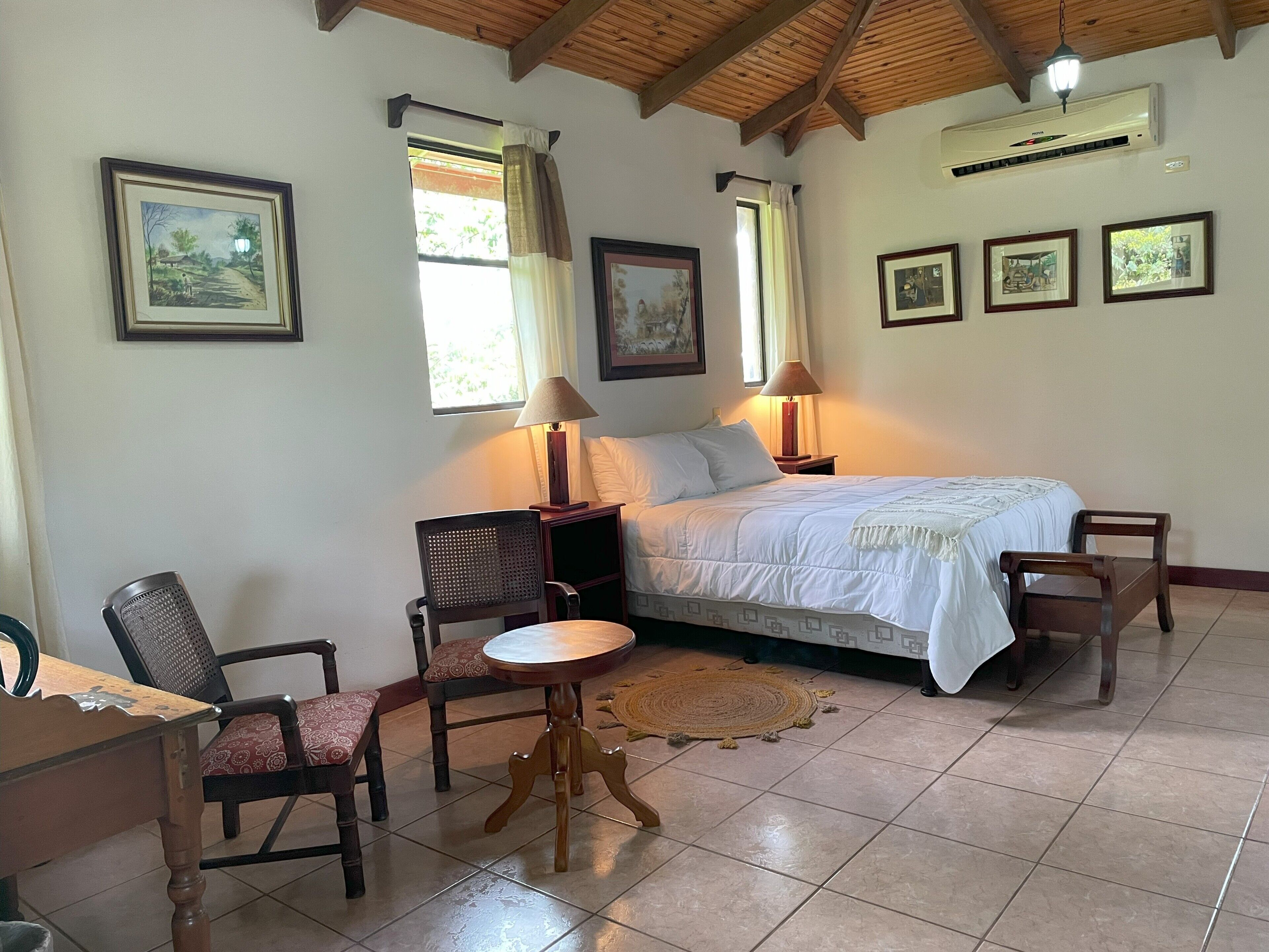 Ein Schlafzimmer mit einem Bett, zwei Stühlen, einem kleinen Tisch und einem Fenster mit Vorhängen.