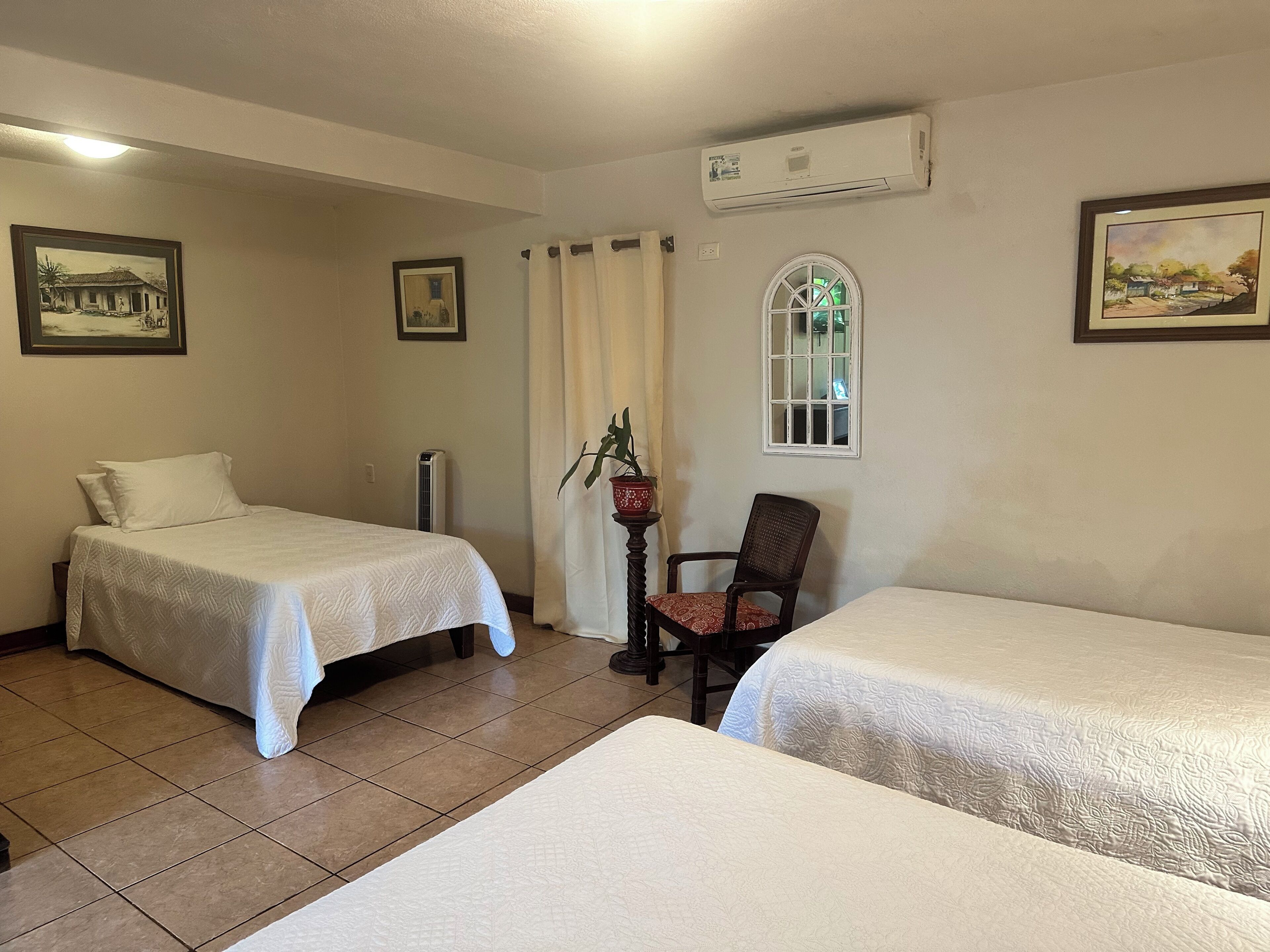 A hotel room with two beds, a chair, a window, and a wall-mounted air conditioner.