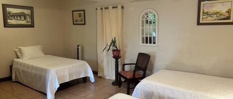 A hotel room with two beds, a chair, a window, and a wall-mounted air conditioner.