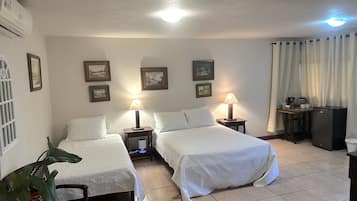 Une chambre d’hôtel avec deux lits, un bureau, un réfrigérateur et une plante en pot.