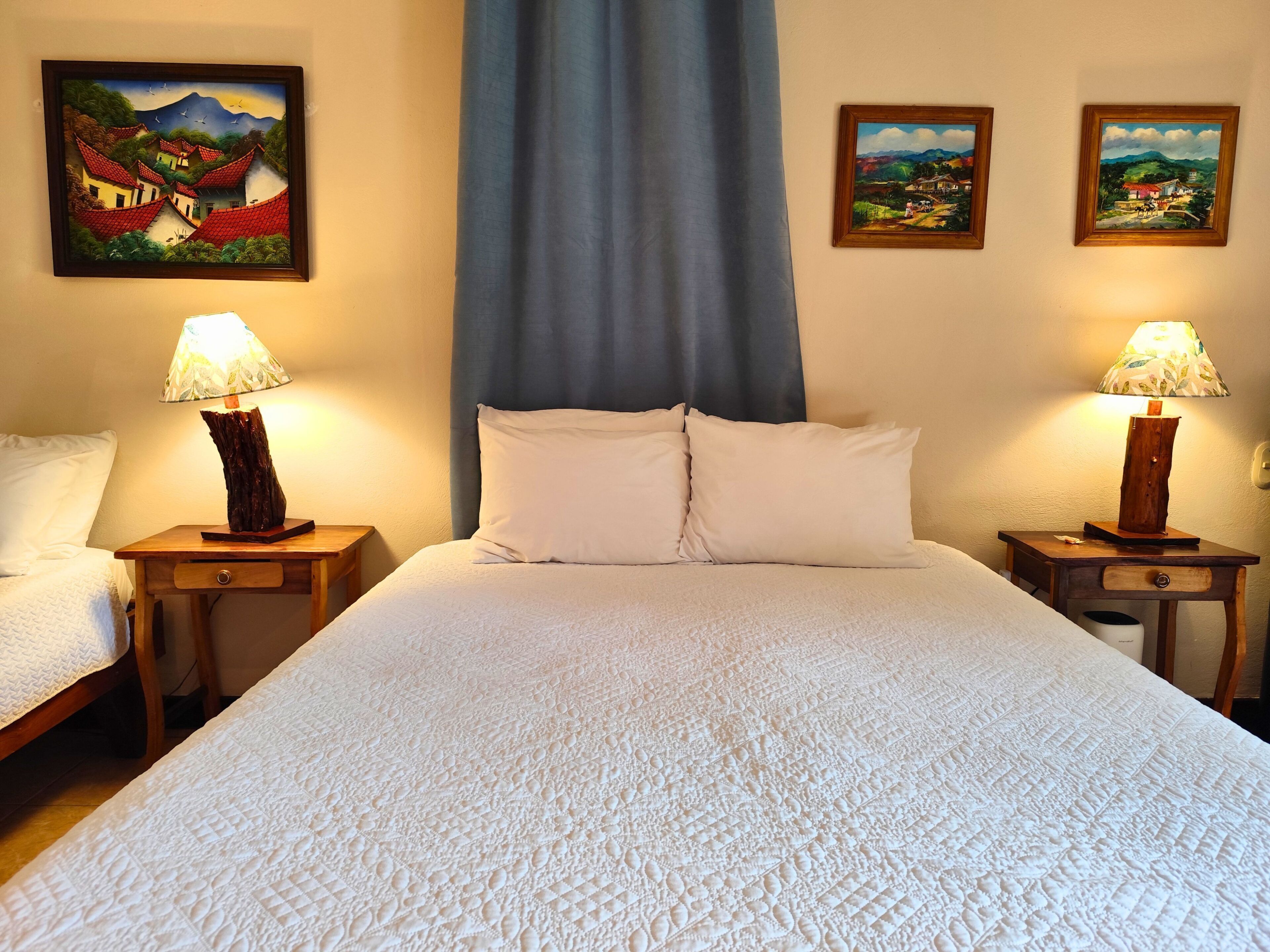 Een hotelkamer met een groot bed, twee nachtkastjes met lampen, en drie ingelijste schilderijen aan de muur.