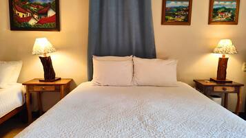 A hotel room with a large bed, two bedside tables with lamps, and three framed paintings on the wall.