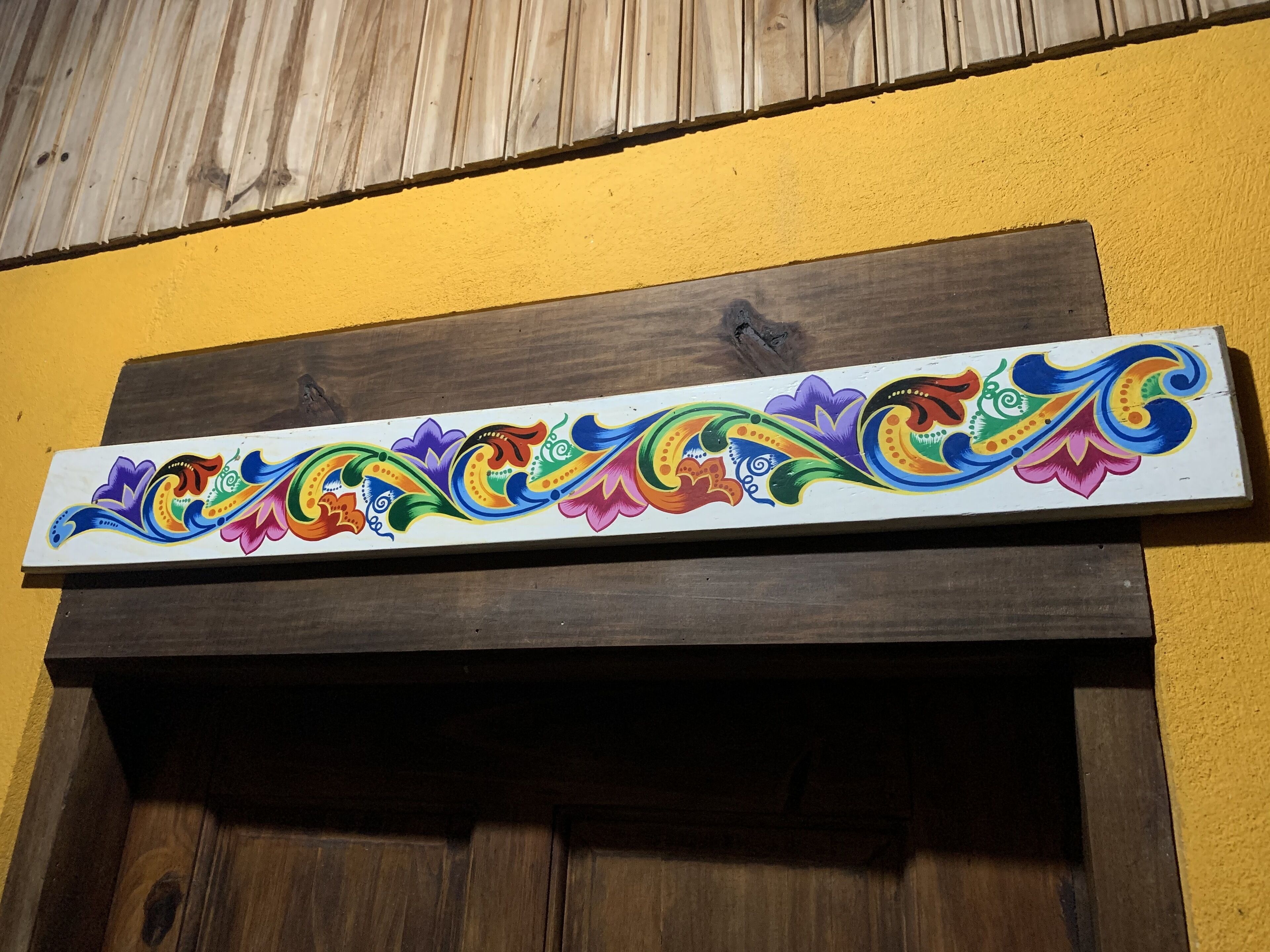 Een kleurrijk decoratief paneel met ingewikkelde ontwerpen, bevestigd aan een houten constructie voor een gele muur.