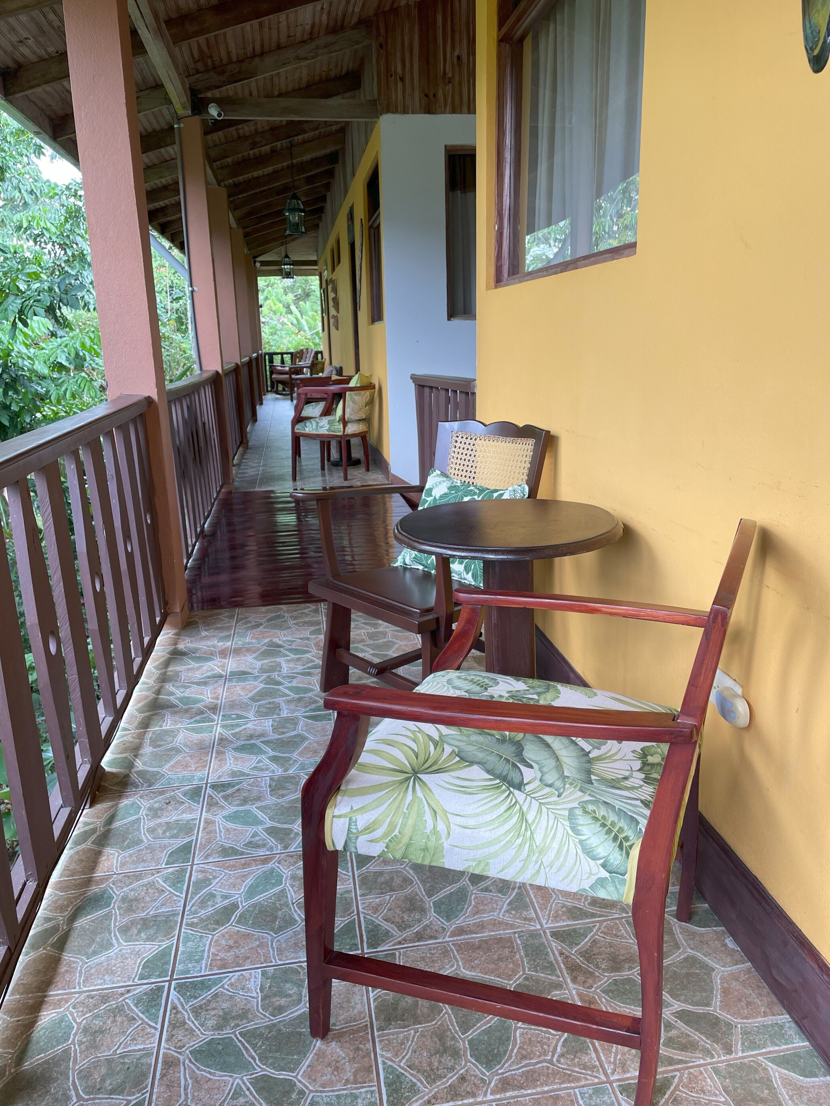 A covered outdoor seating area with wooden furniture and a tiled floor.