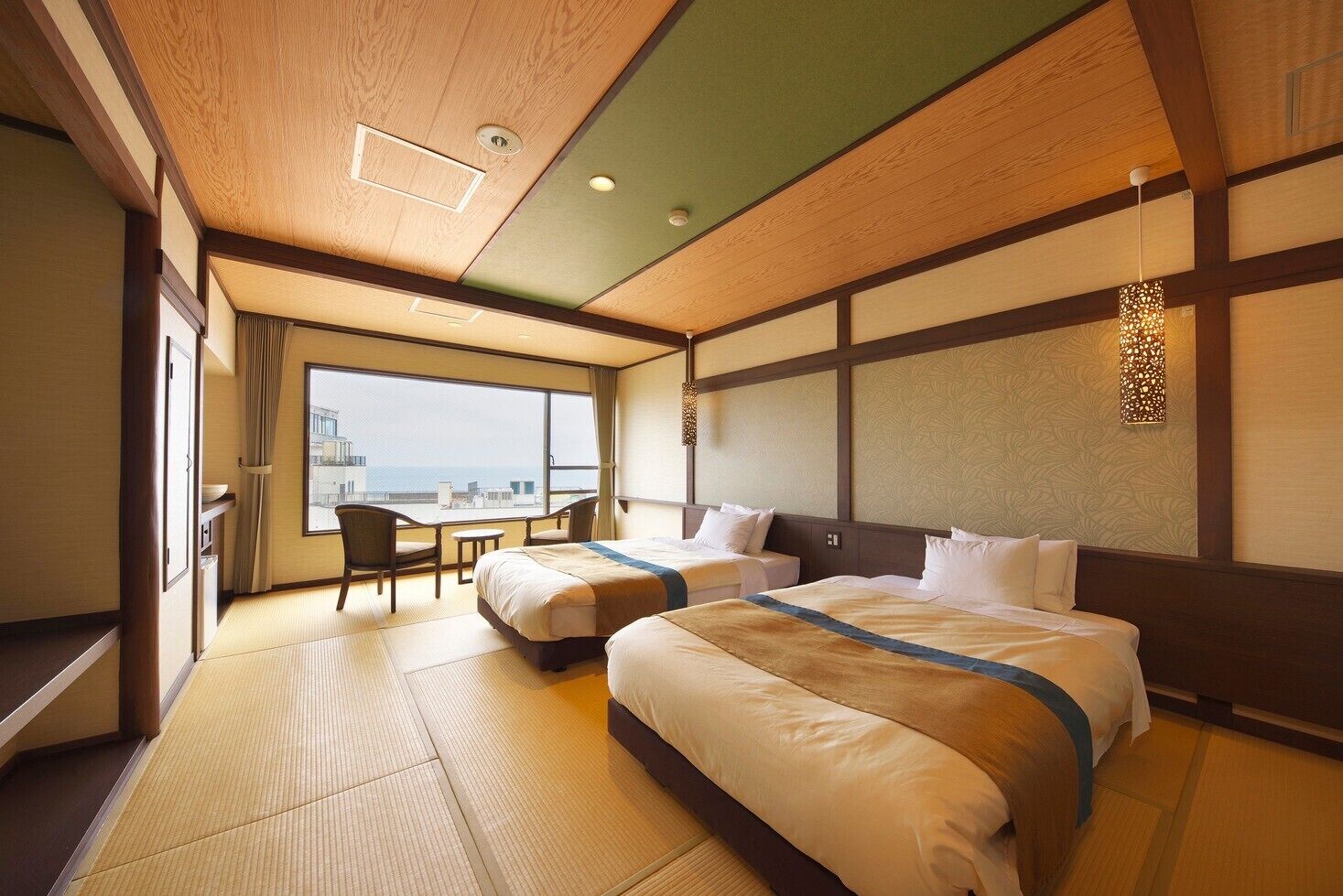 Habitación de hotel con dos camas, zona de estar con sillas, ventana grande con vistas y techo de estilo japonés tradicional.