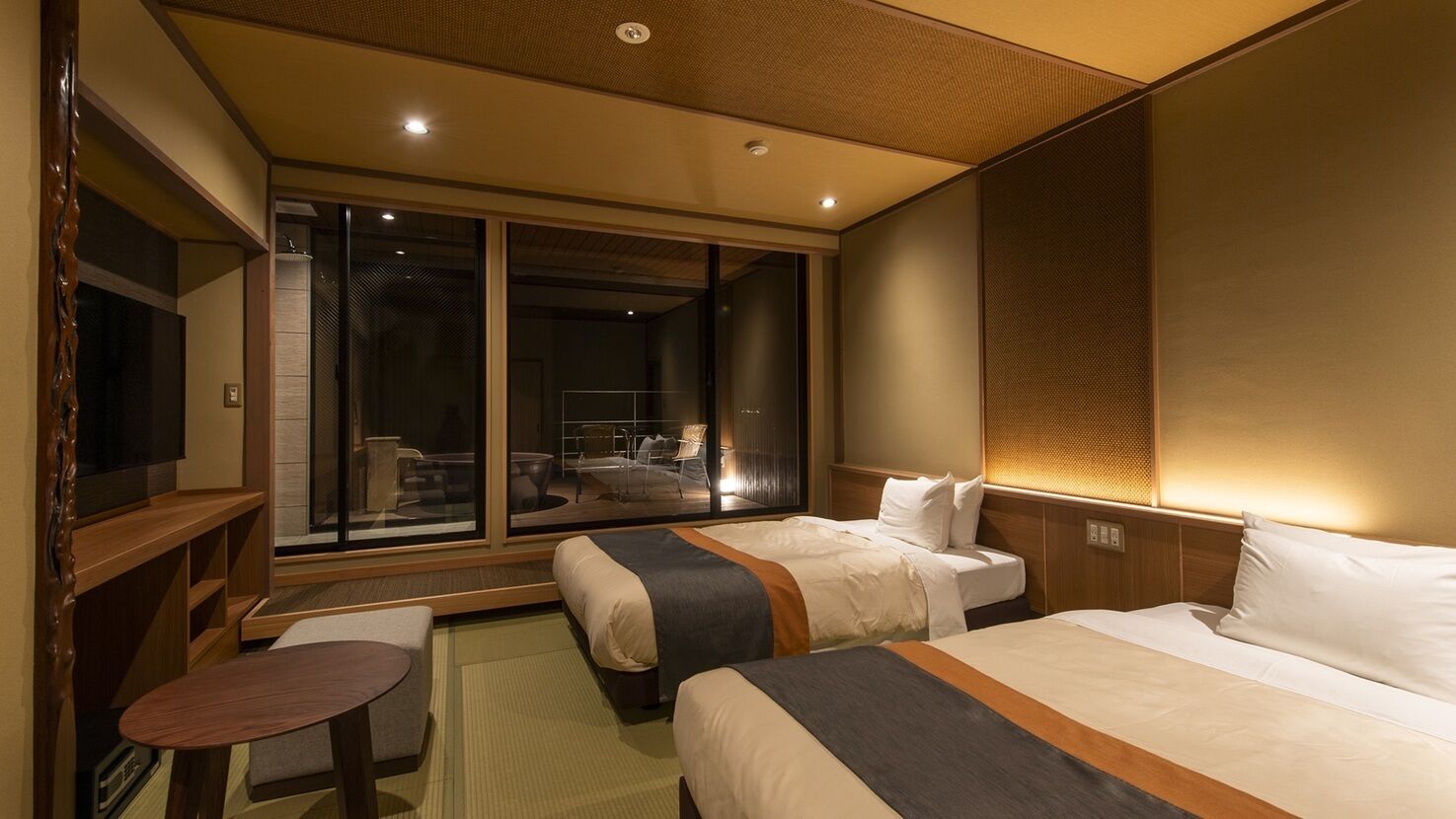 A hotel room with two beds, a TV, a small table, and a sliding glass door leading to a balcony.