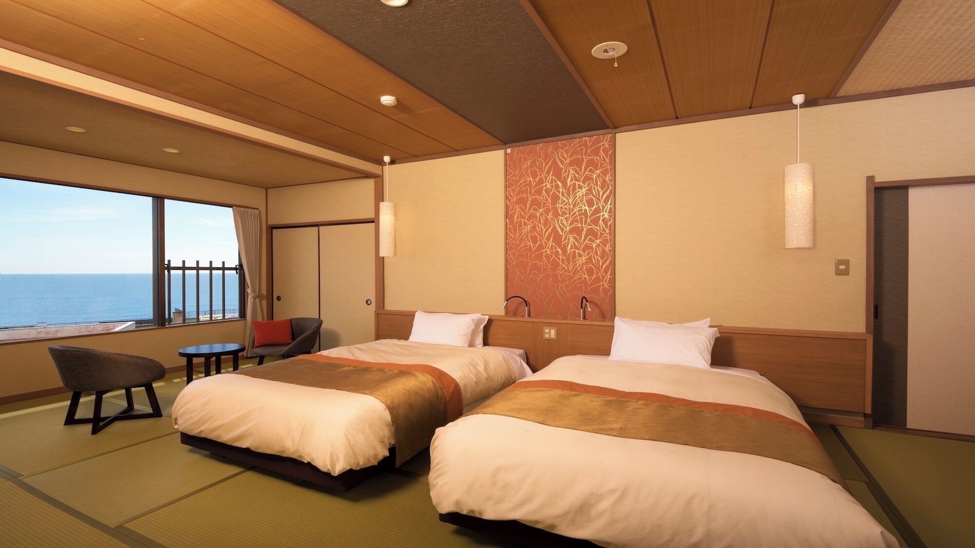A hotel room with two beds, a view of the sea, a small table, and a chair.