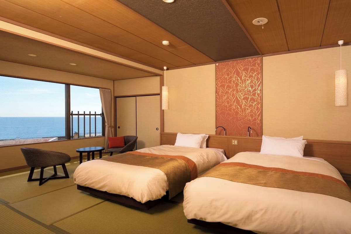 A hotel room with two beds, a view of the sea, a small table, and a chair.