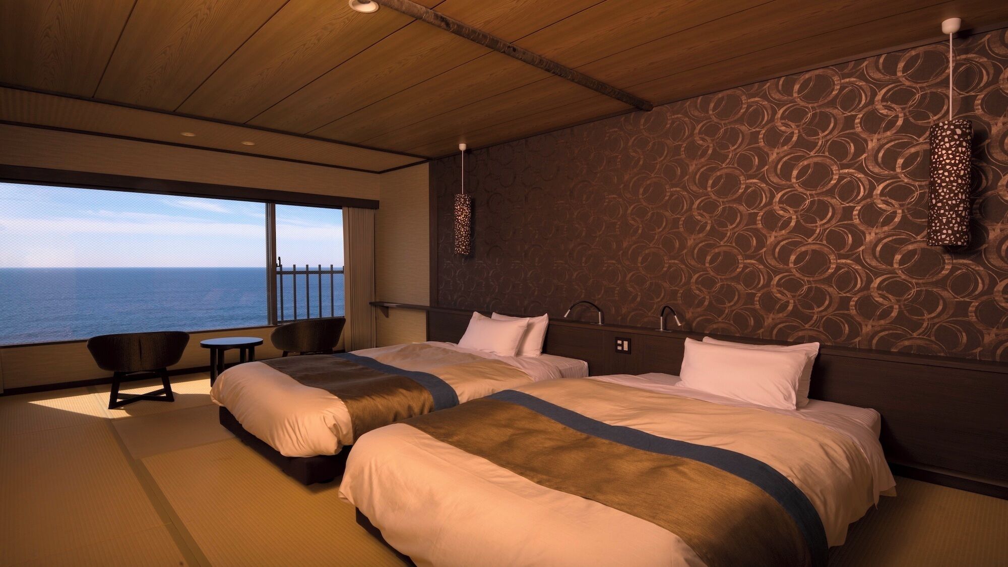 A hotel room with two beds, a view of the sea, a small table, and a chair.