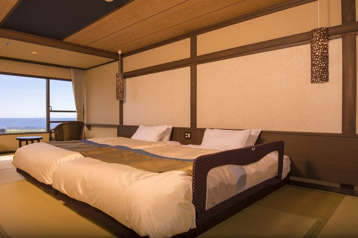 Ett hotellrum med en stor säng, en stol, ett litet bord och utsikt över havet.