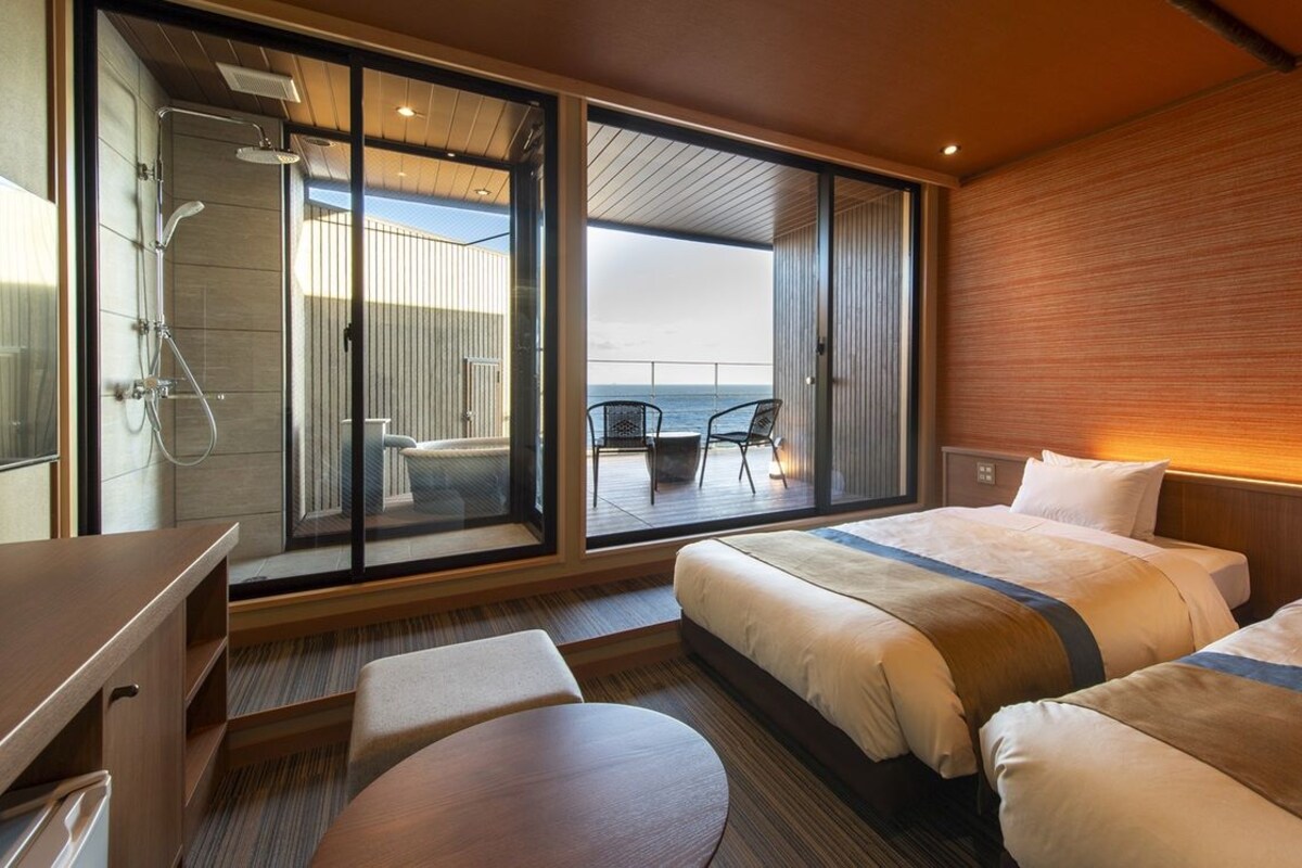 Een moderne hotelkamer met een balkon, douche, bed, bureau en stoel.