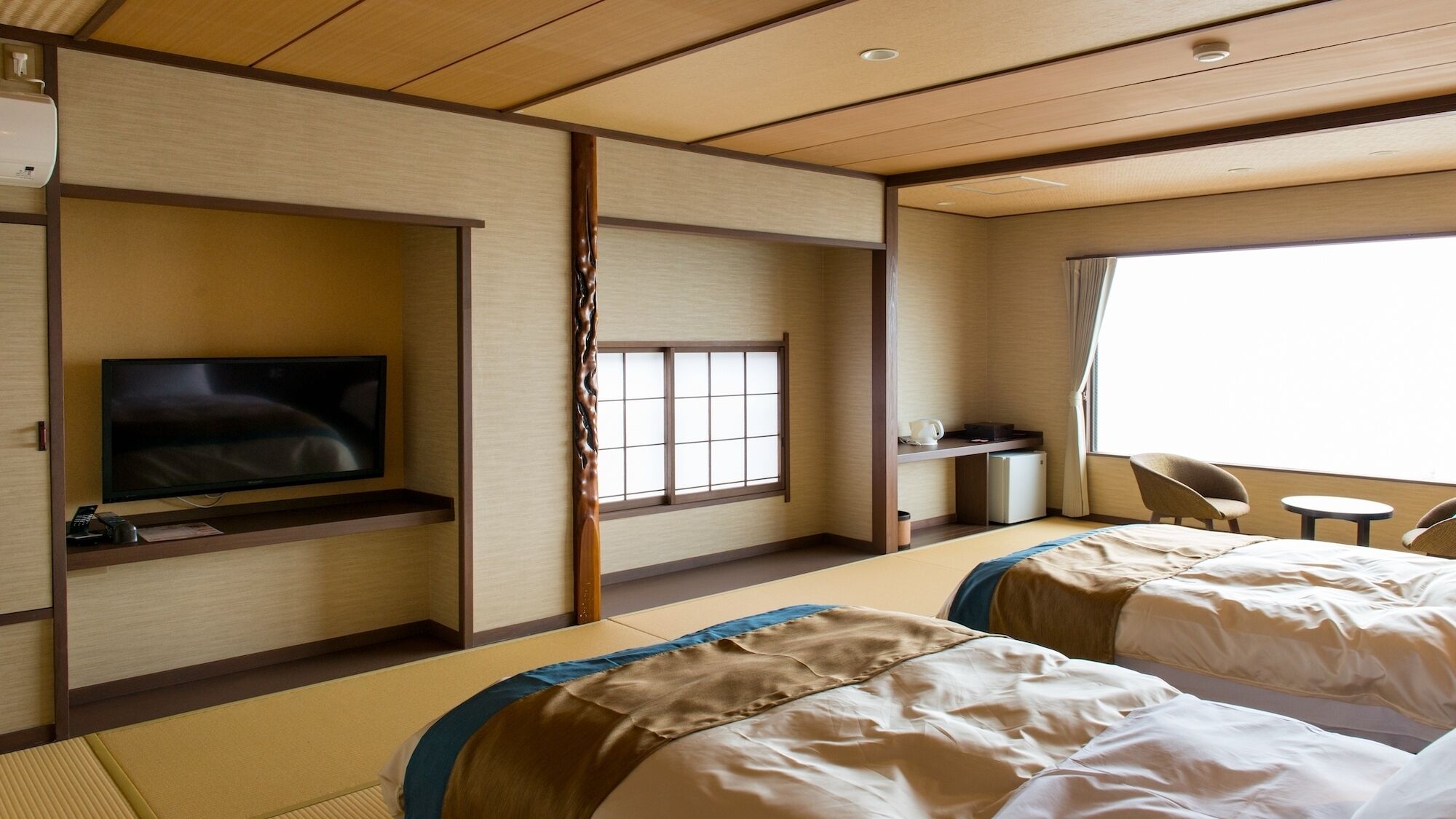 A hotel room with a television, two beds, a desk, a small refrigerator, and a window.