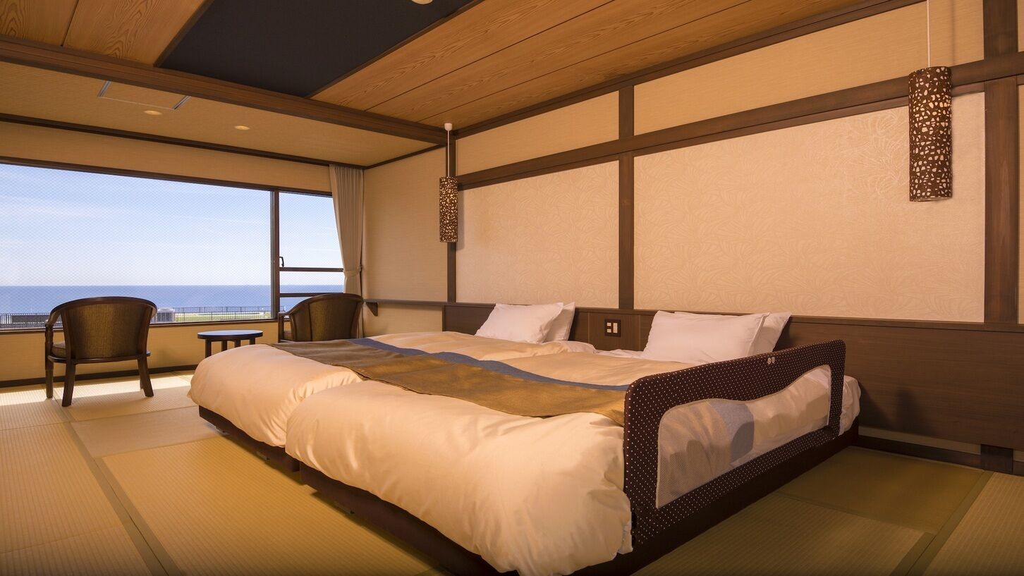 A hotel room with a large bed, a chair, a small table, and a view of the ocean.