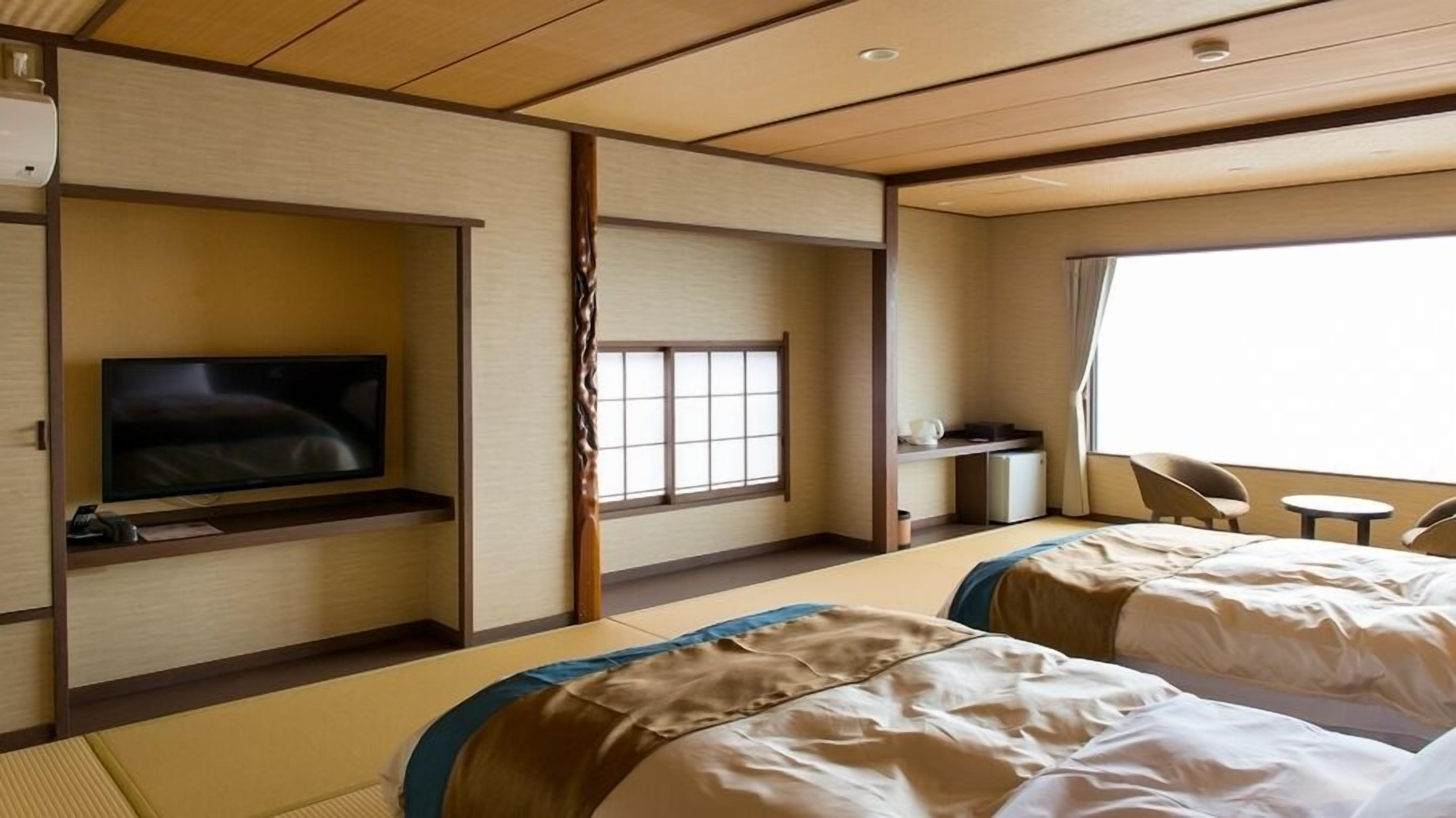 Una habitación de hotel con televisión, dos camas, escritorio y ventana.