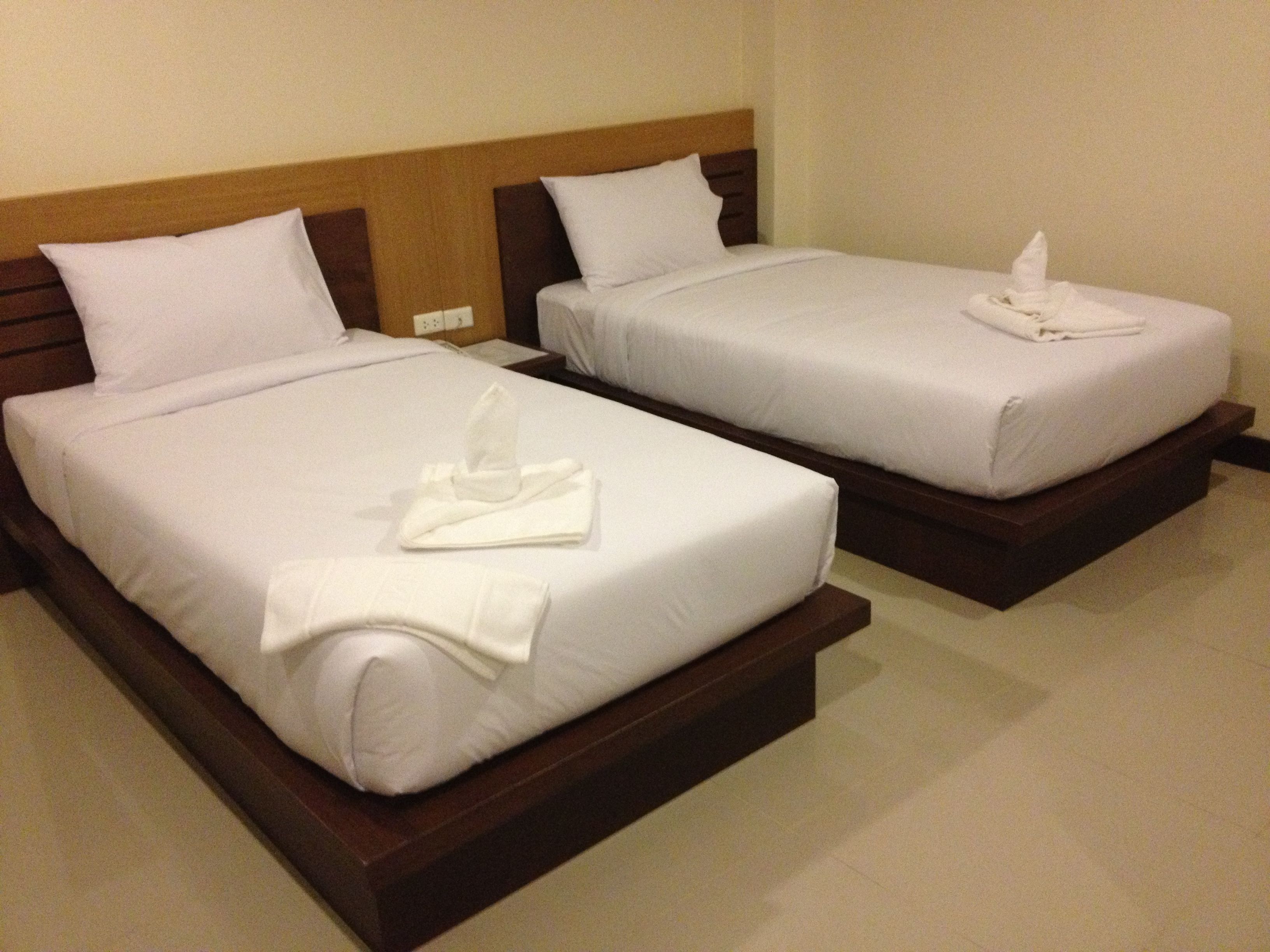 Dos camas individuales con sábanas blancas y cabeceras de madera en una habitación de hotel.