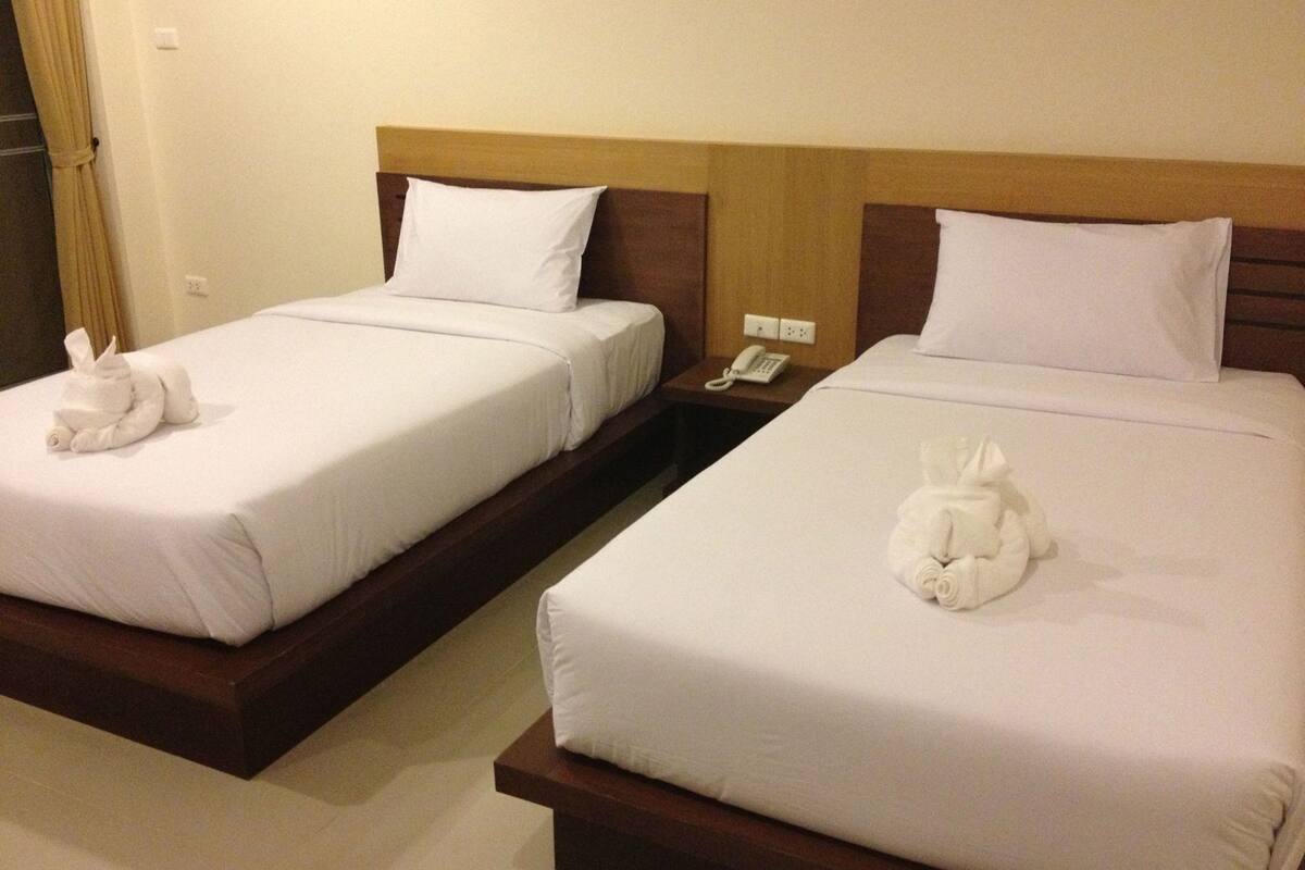 Two twin beds with white linens, a wooden headboard, a bedside table with a phone, and a towel sculpture on each bed.