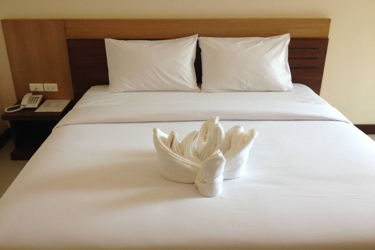 A neatly made bed with white linens and a towel arrangement in the center.