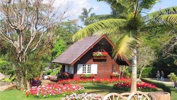 A wooden cabin with a sloped roof, surrounded by lush greenery and colorful flowers. - Khunnam Rimtarn Resort (Mae Sai)