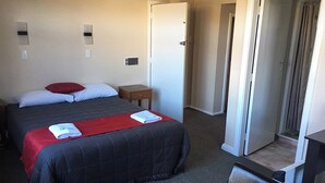 Een hotelkamer met een bed, een klein tafeltje, een stoel en een deur die naar een andere kamer leidt.