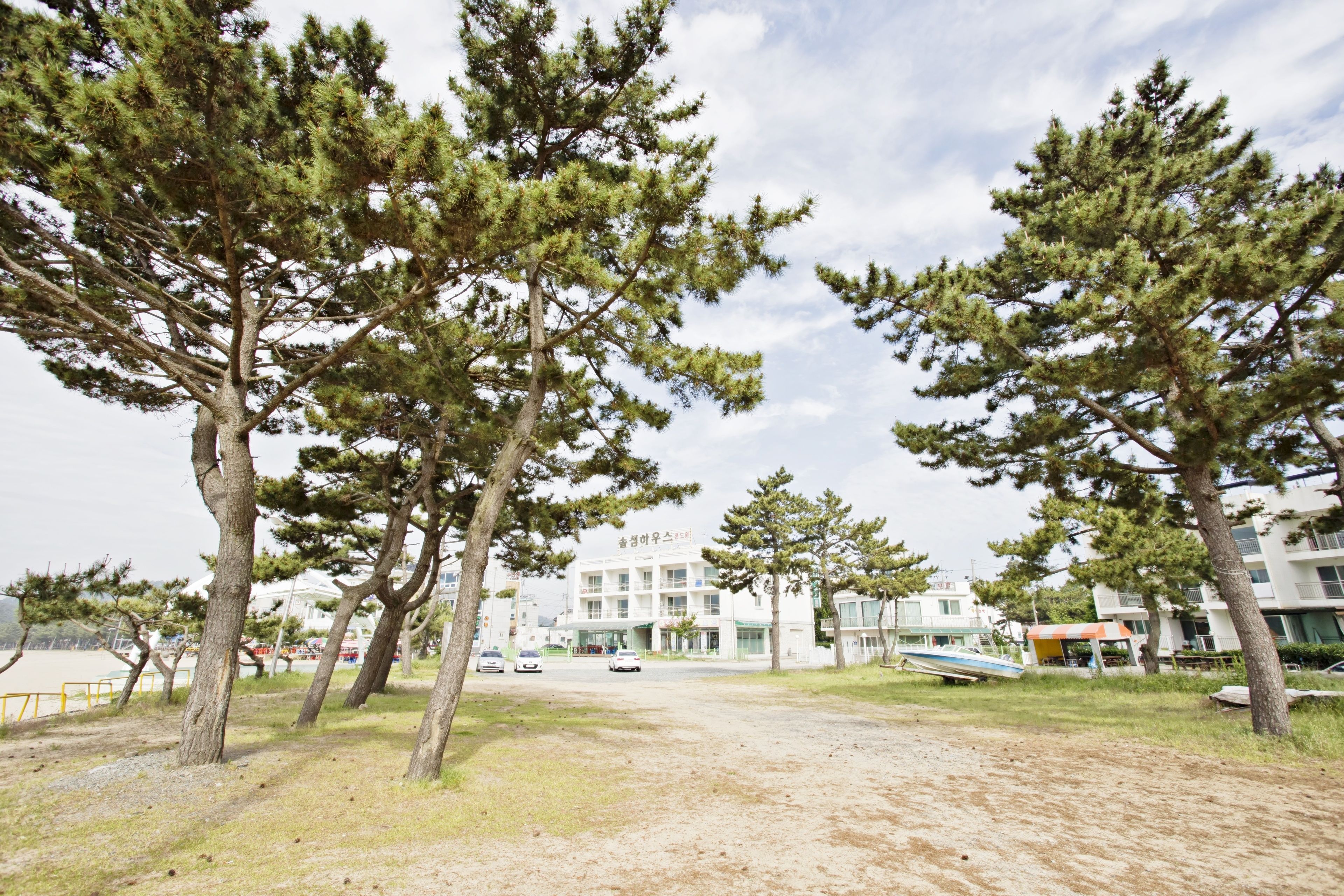 A building with a sign in a foreign language, surrounded by trees and a dirt path.