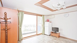 Ein Zimmer mit einer Schiebeglastür, die auf einen Balkon führt, einem Holz-Kleiderständer, einem Fernseher auf einem Holzboden und einer weißen Klimaanlage an der Wand.