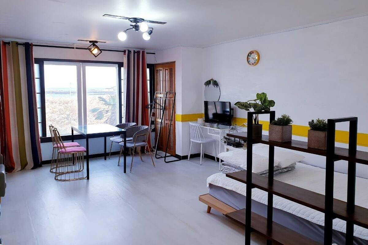 Ein Zimmer mit Bett, Schreibtisch, Stuhl, Fernseher und einem Fenster mit Vorhängen.