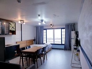 A compact hotel room with a kitchenette, a dining area, a bed, and a large window with curtains. - Morning Beach Pension (Jeju City)