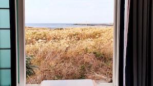A view through a window with a coastal landscape, including dry grass and a distant body of water. - Morning Beach Pension (Jeju City)