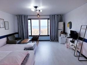 A hotel room with a bed, a desk, a chair, a TV, and a view of the beach.