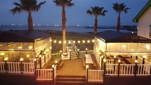 A beachfront property with a wooden deck, white railings, and string lights. - Morning Beach Pension (Jeju City)