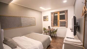 Une chambre d’hôtel avec un lit, un bureau avec un ordinateur portable, une chaise, une télévision et une fenêtre avec des rideaux.