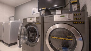 A laundry facility with multiple washing machines, a television mounted on the wall, and a digital display on the machines. - Hotel Major 2 (Jeju City)