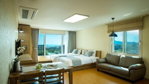 Una habitación de hotel moderna con dos camas, un sofá, un comedor con mesa y sillas, y ventanas amplias con vistas al paisaje.