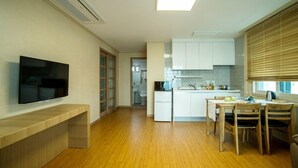 Una cocina moderna con armarios blancos, un comedor con sillas de madera y un televisor montado en la pared.