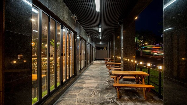 Un espacio al aire libre cubierto con suelo de piedra y mesas de madera, con vistas a una calle con luces que se mueven.