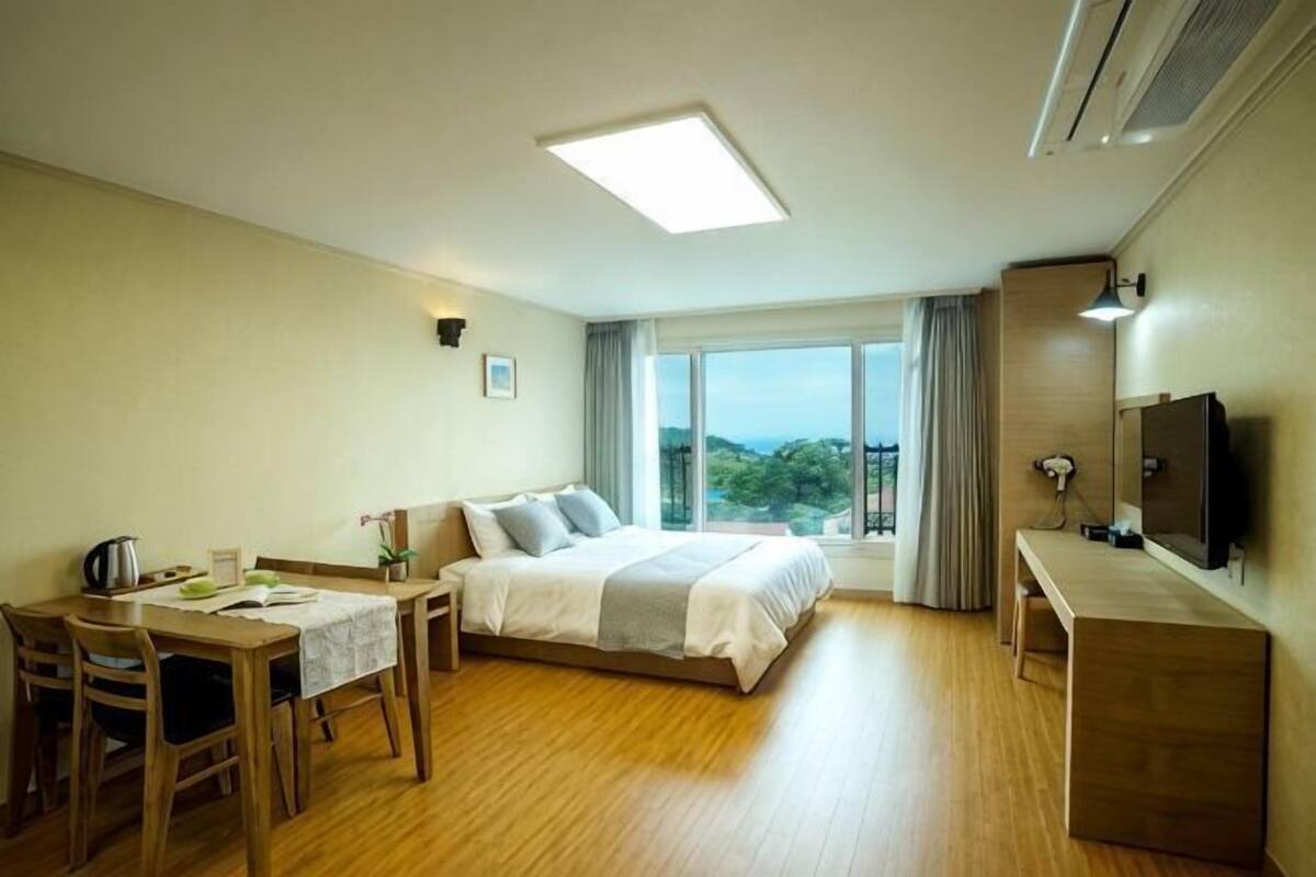Quarto de hotel com cama, escrivaninha, cadeira, televisão e janela com vista.