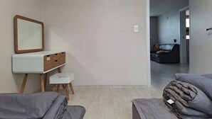 Une chambre à coucher au style minimaliste, avec un lit, une table de chevet dotée d’un miroir et un petit tabouret.