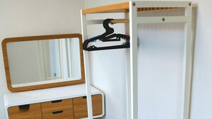 Une pièce avec un bureau blanc, un miroir, une étagère en bois et un lit.