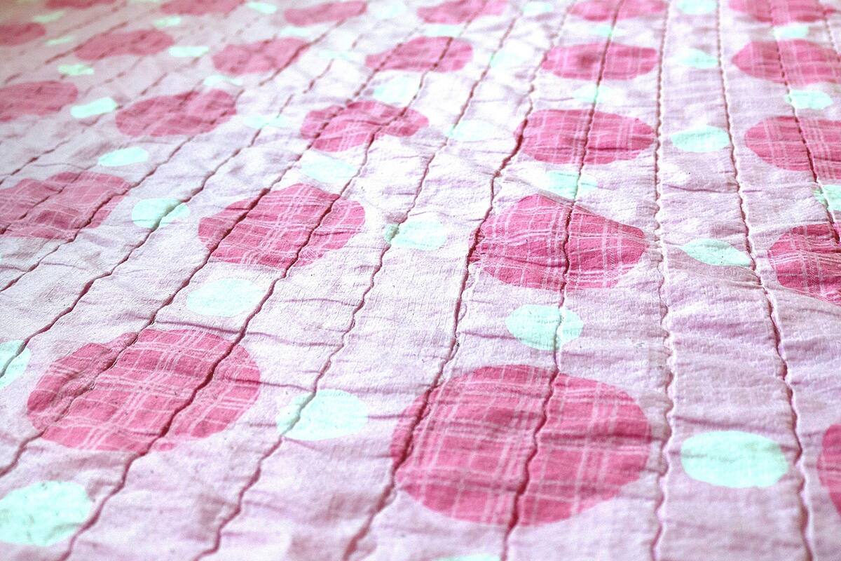 Ein Bett mit einer zweiseitigen Bettdecke in Rosa und Weiß, einem Kissen in Rosa und einem Fenster mit Vorhang.