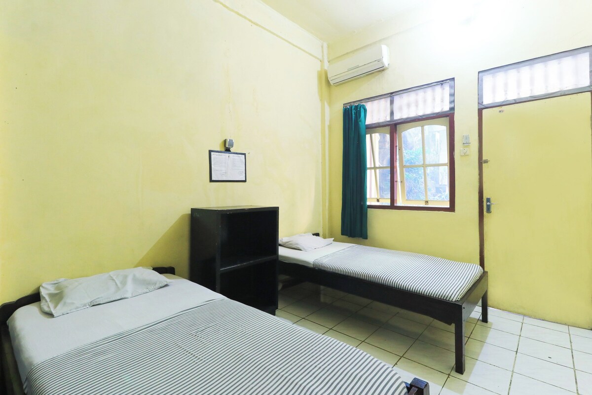 Un dormitorio con dos camas individuales, un escritorio pequeño, una ventana con cortinas y una puerta.