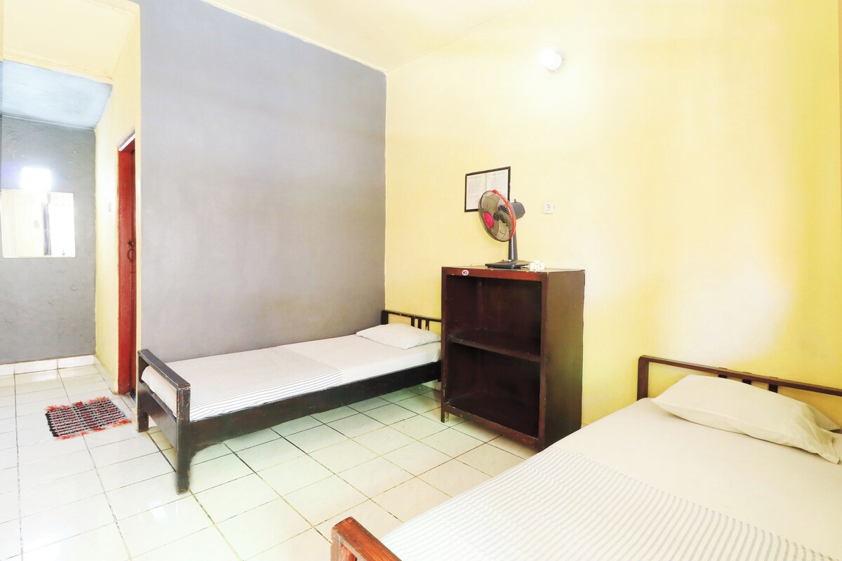 Une chambre avec deux lits, un ventilateur et une étagère.