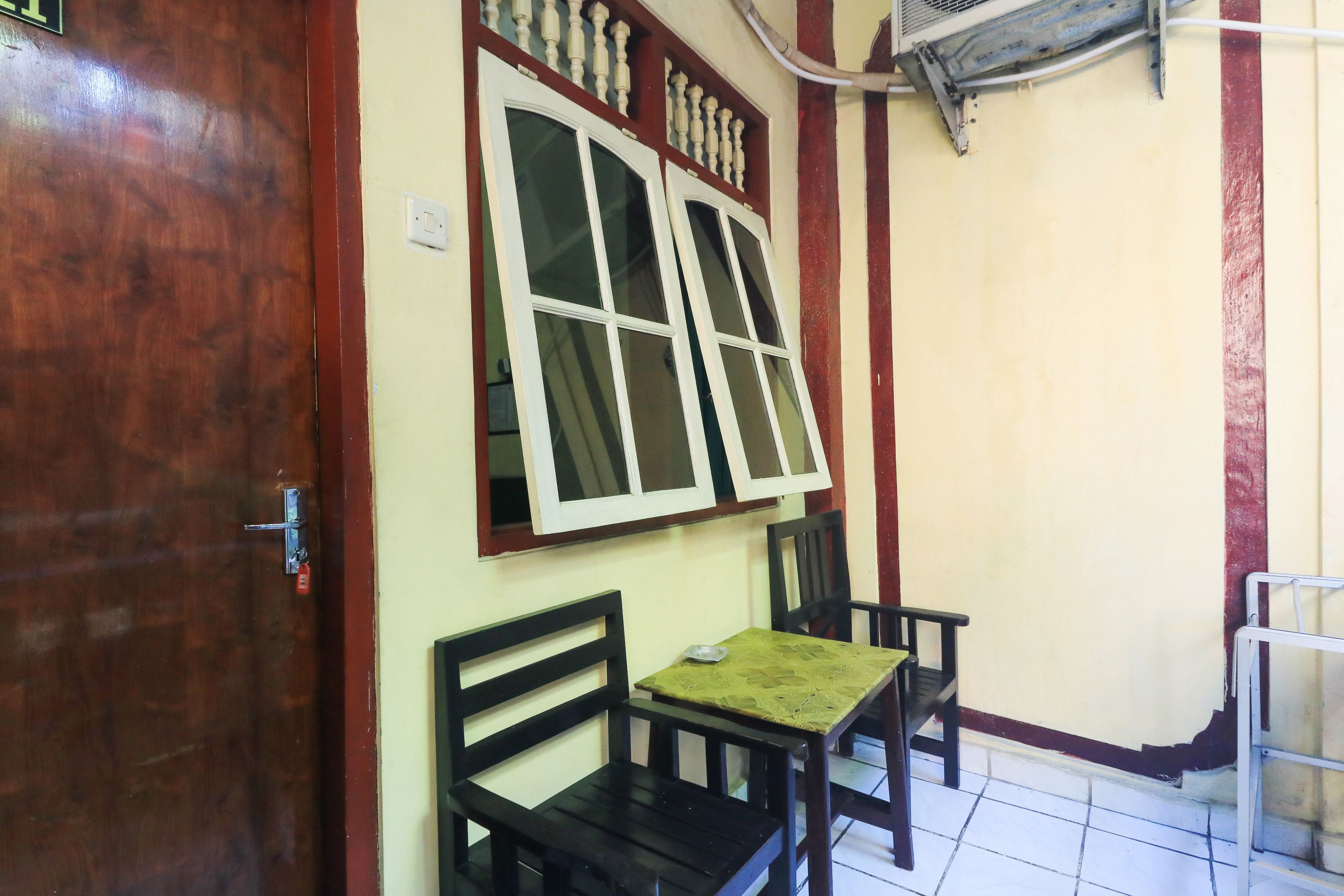 A room with a wooden door, a window with white frames, a table with a green tablecloth, and two black chairs.