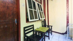A room with a wooden door, a window with white frames, a table with a green tablecloth, and two black chairs. - Bali Duta Wisata Beach Inn (Kuta)