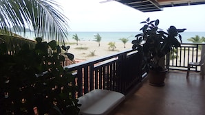 Un balcone con vista sulla spiaggia, una sedia bianca e piante in vaso.