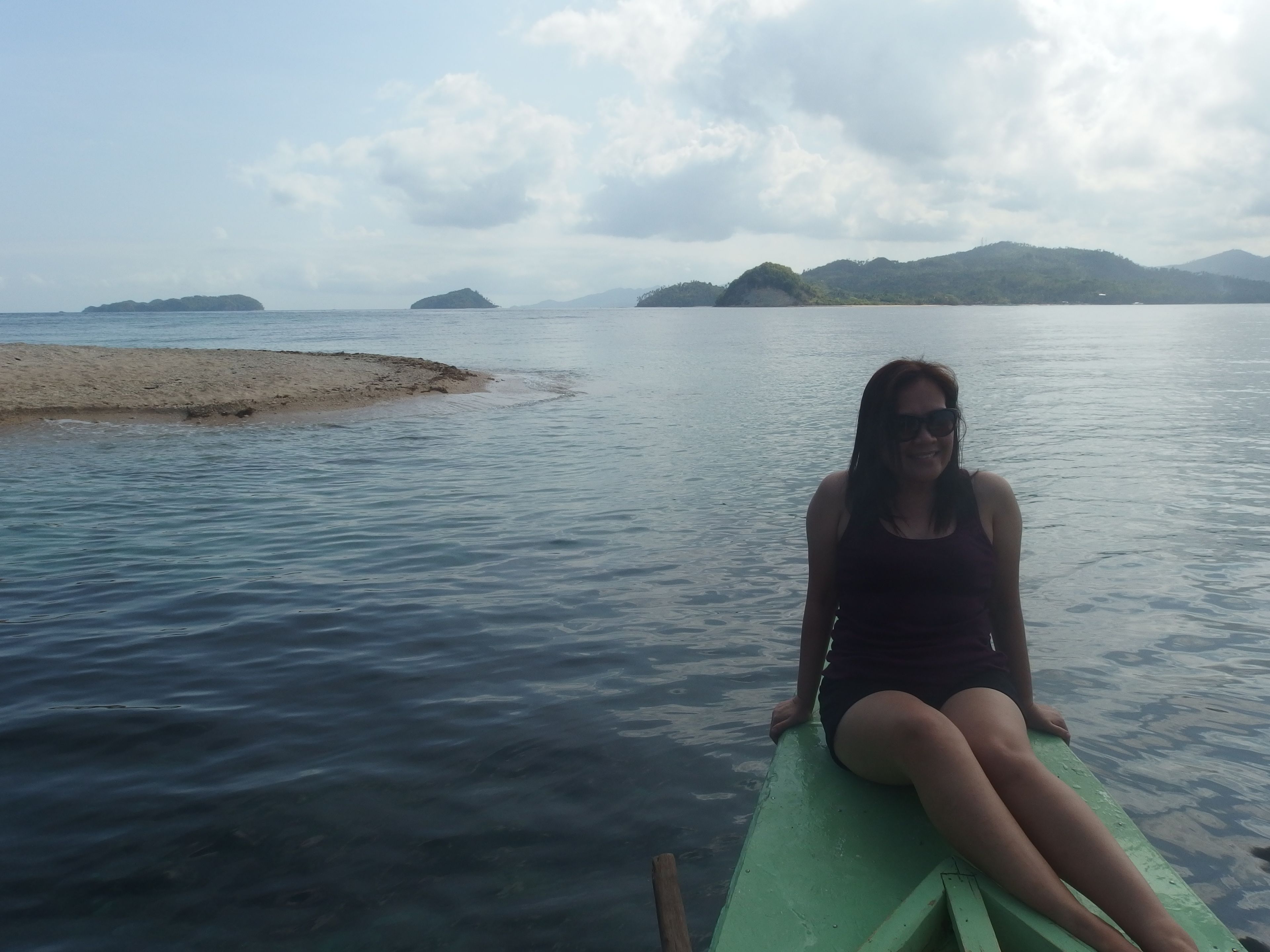 A person sitting on a green boat in calm waters with distant islands and a clear sky.