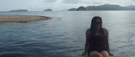 A person sitting on a green boat in calm waters with distant islands and a clear sky.