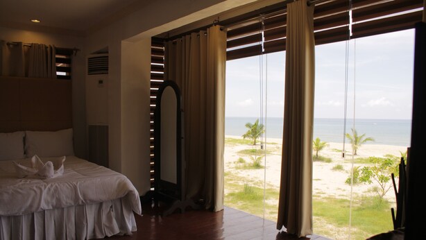 Una camera da letto con un letto grande, vista sulla spiaggia e una finestra con tende.