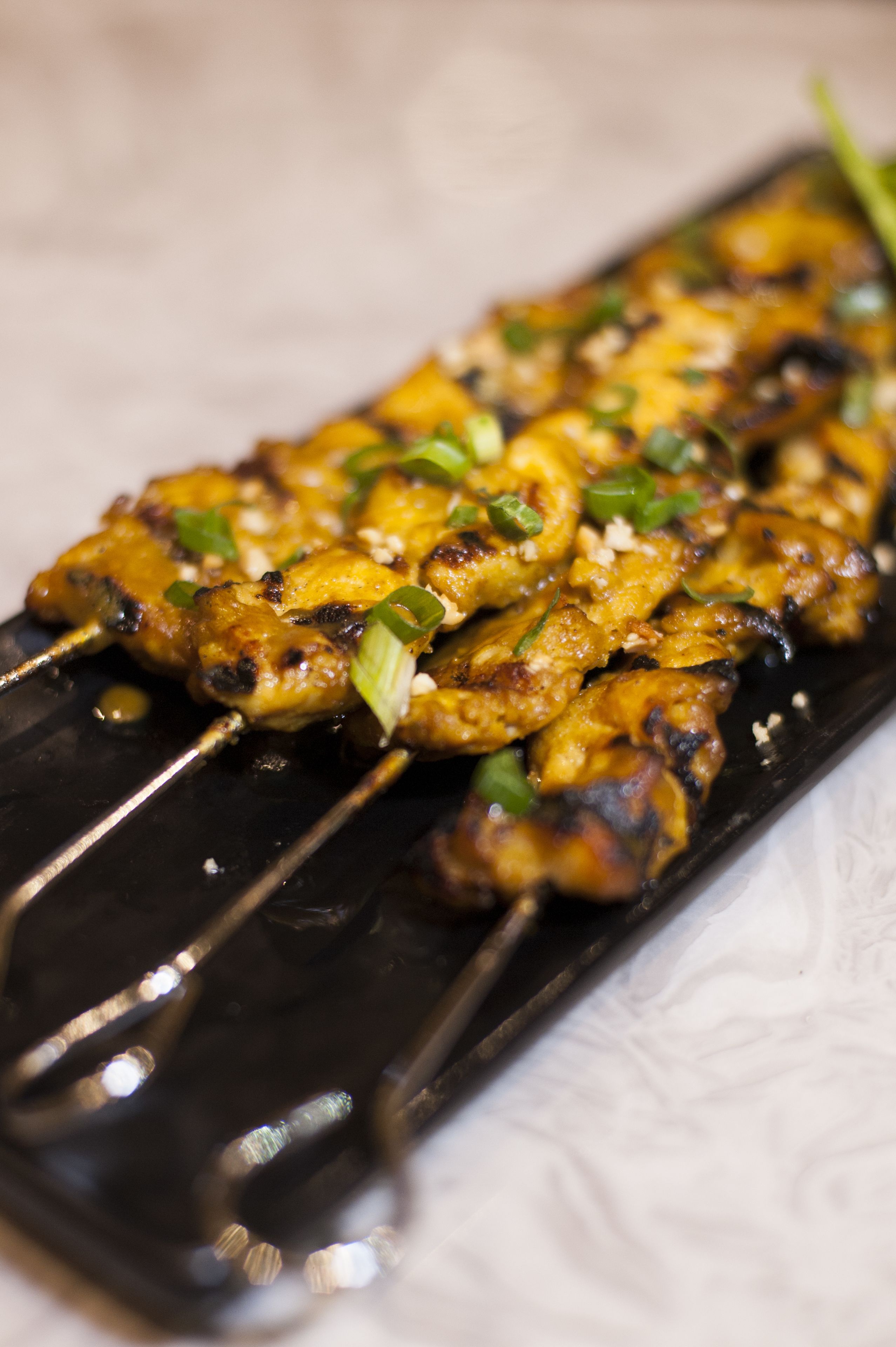 A close-up of grilled chicken skewers garnished with green onions on a black plate.