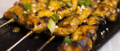 A close-up of grilled chicken skewers garnished with green onions on a black plate.